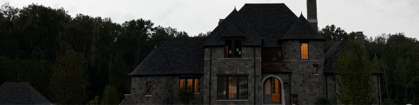 Stone custom home with a steep roofline and arched entry at dusk